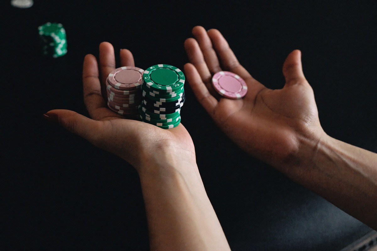 A young couple sharing one stool at a slot machine, the woman pointing at a small bonus panel on the screen while the man counts a thin stack of notes