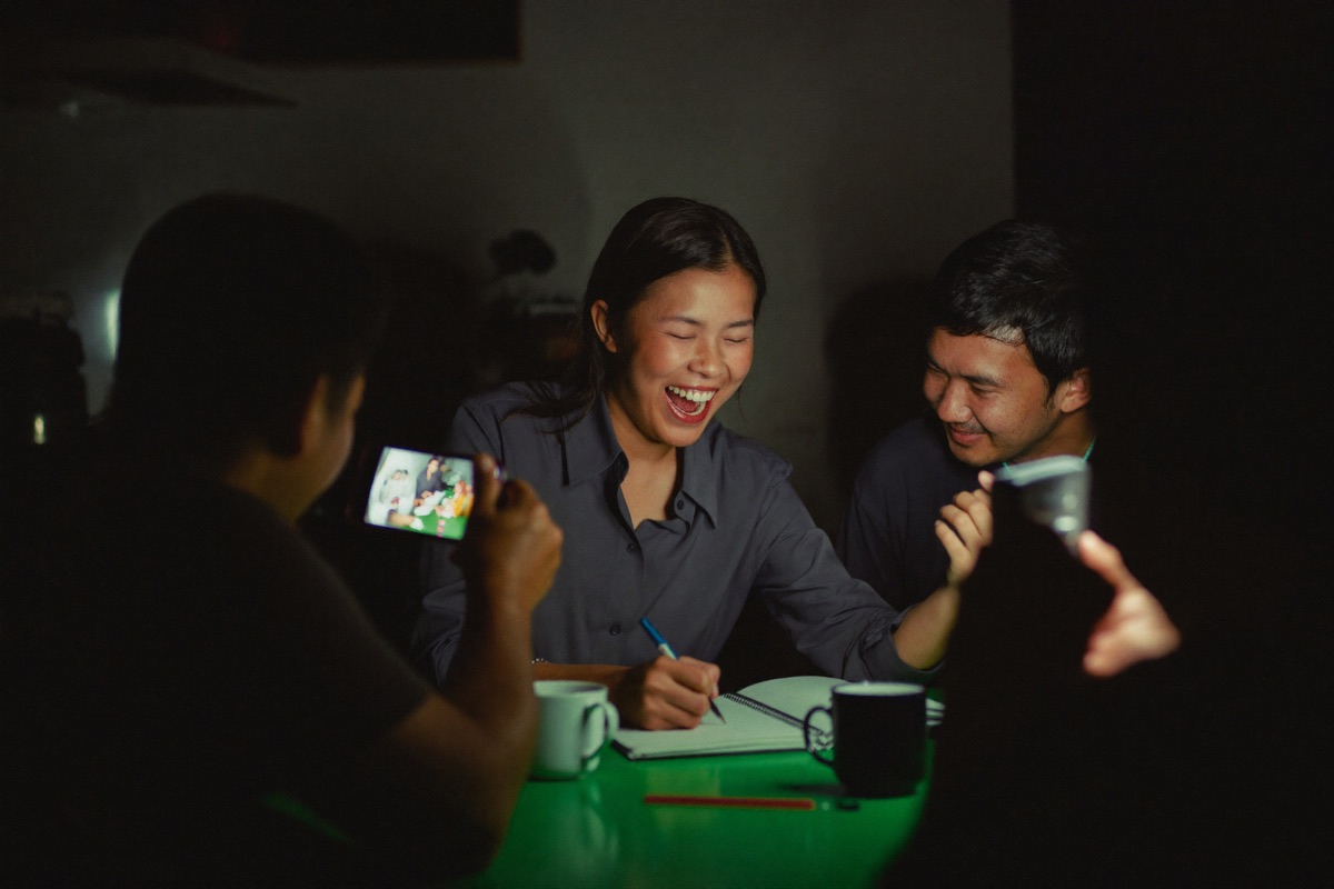 A new player at the cash desk filling in a short form while a smiling host points at the field, a slot hall visible through the glass behind them