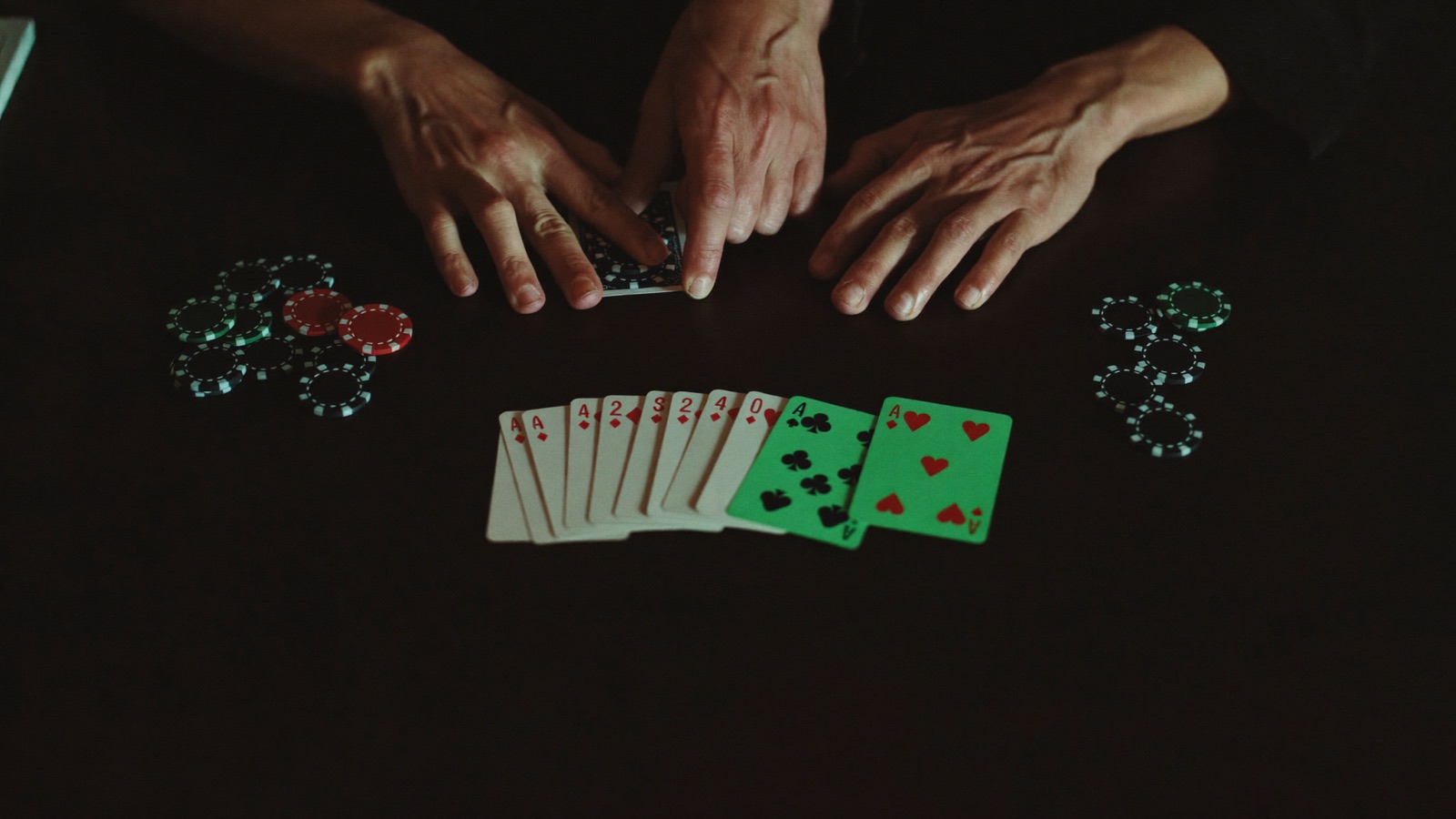 A seated slot player raising both hands as the screen in front of him lights up, a host clapping beside the cabinet